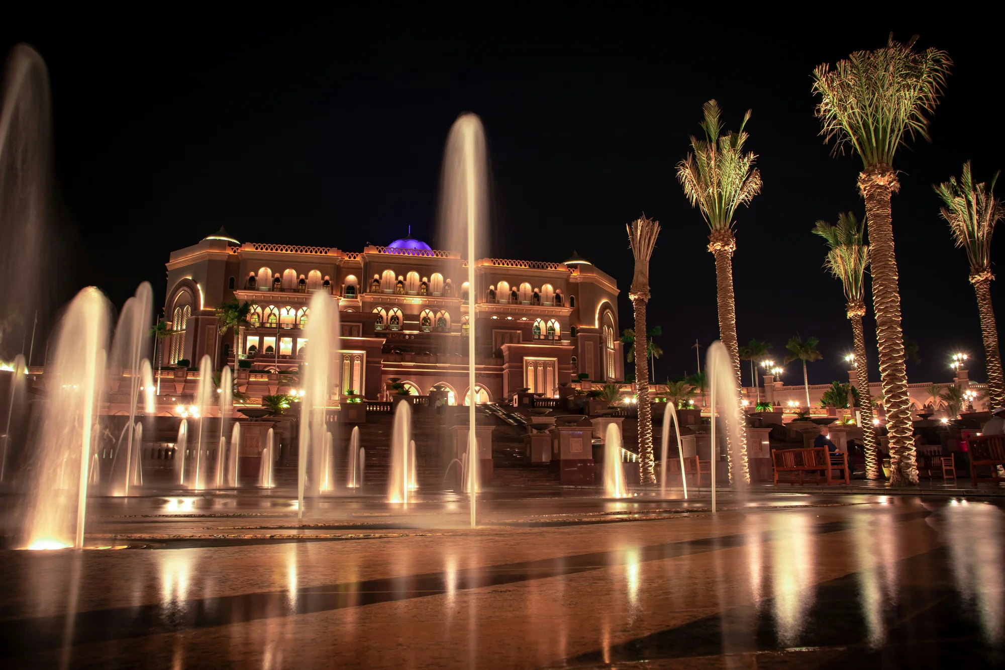 Emirates Palace in Abu Dhabi photographed at night with fountains and palm trees in the background.