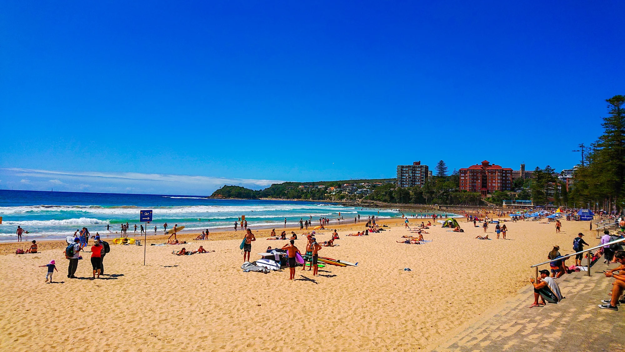 Image of Manly Beach in Sydney with people relaxing on the sand and the blue ocean in the background.