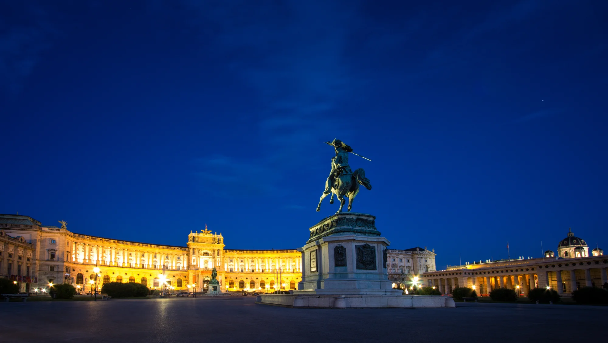 Hofburg Palace in Vienna illuminated at night with statue in the foreground.