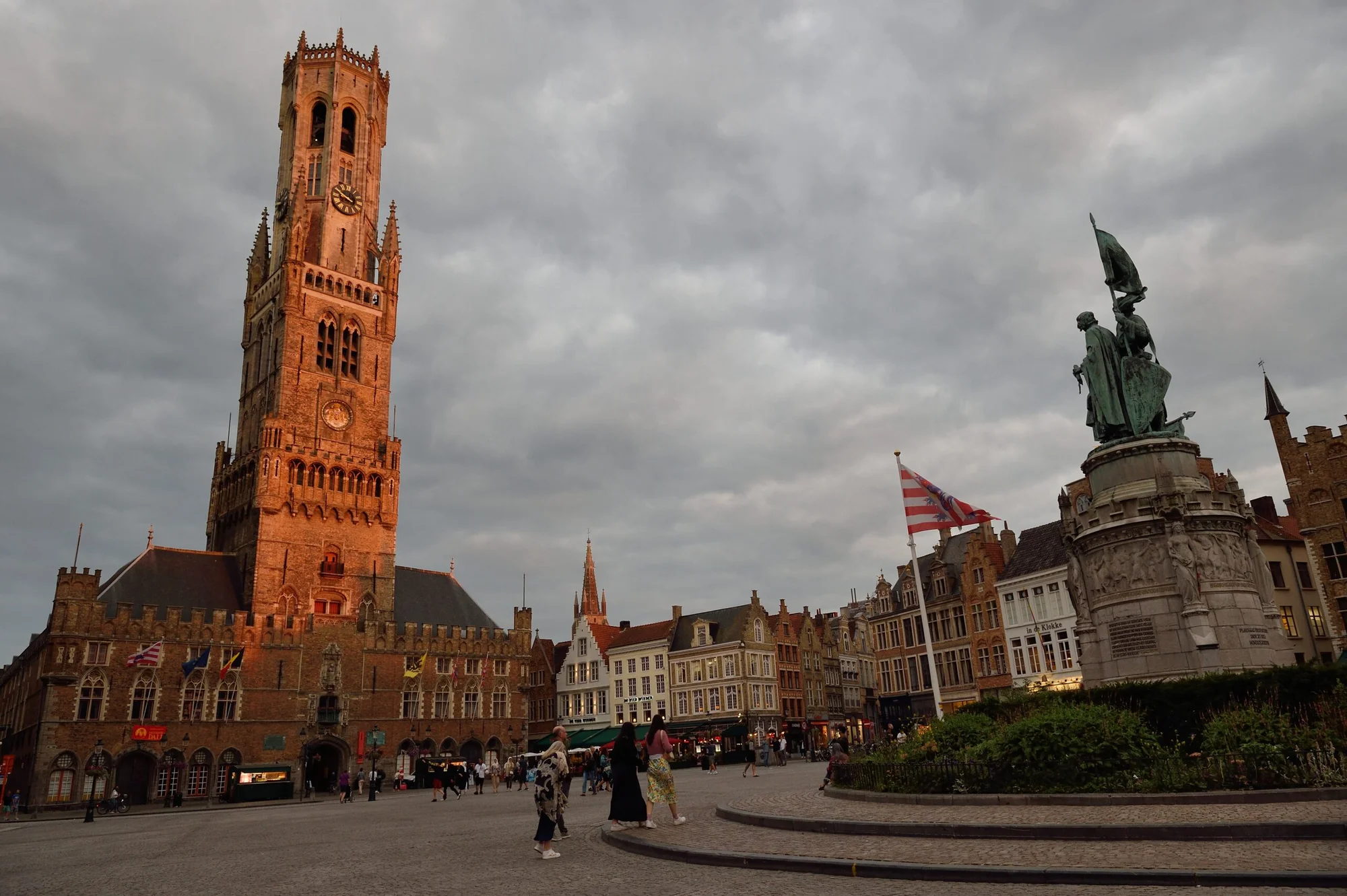 Bruges Market Square at sunset, featuring the Belfry tower and central statue.