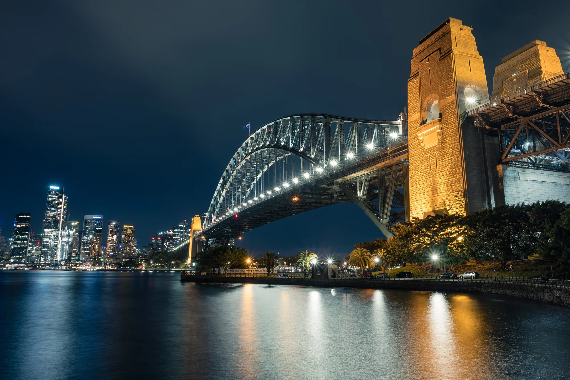 Sydney Harbour Bridge illuminated at night with Sydney's cityscape in the background.