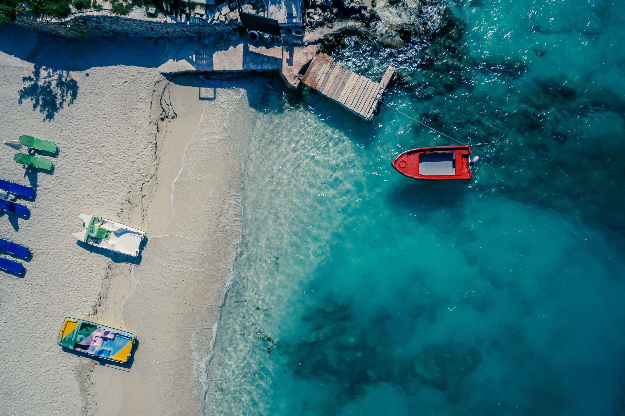 Aerial view of Ksamil Beach with boats on white sand and turquoise water.