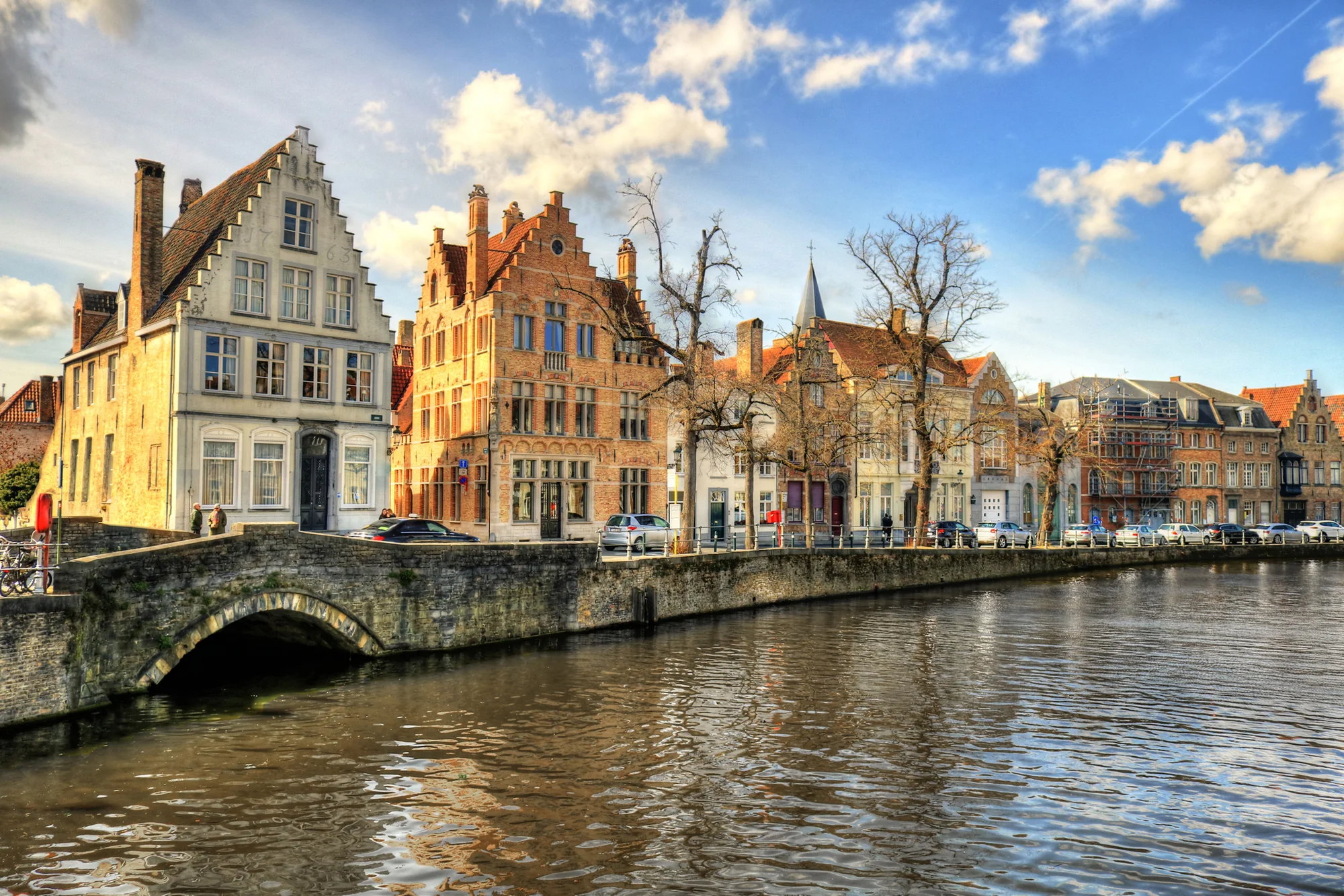 Historic buildings along a canal in Bruges, Belgium, under a blue sky.