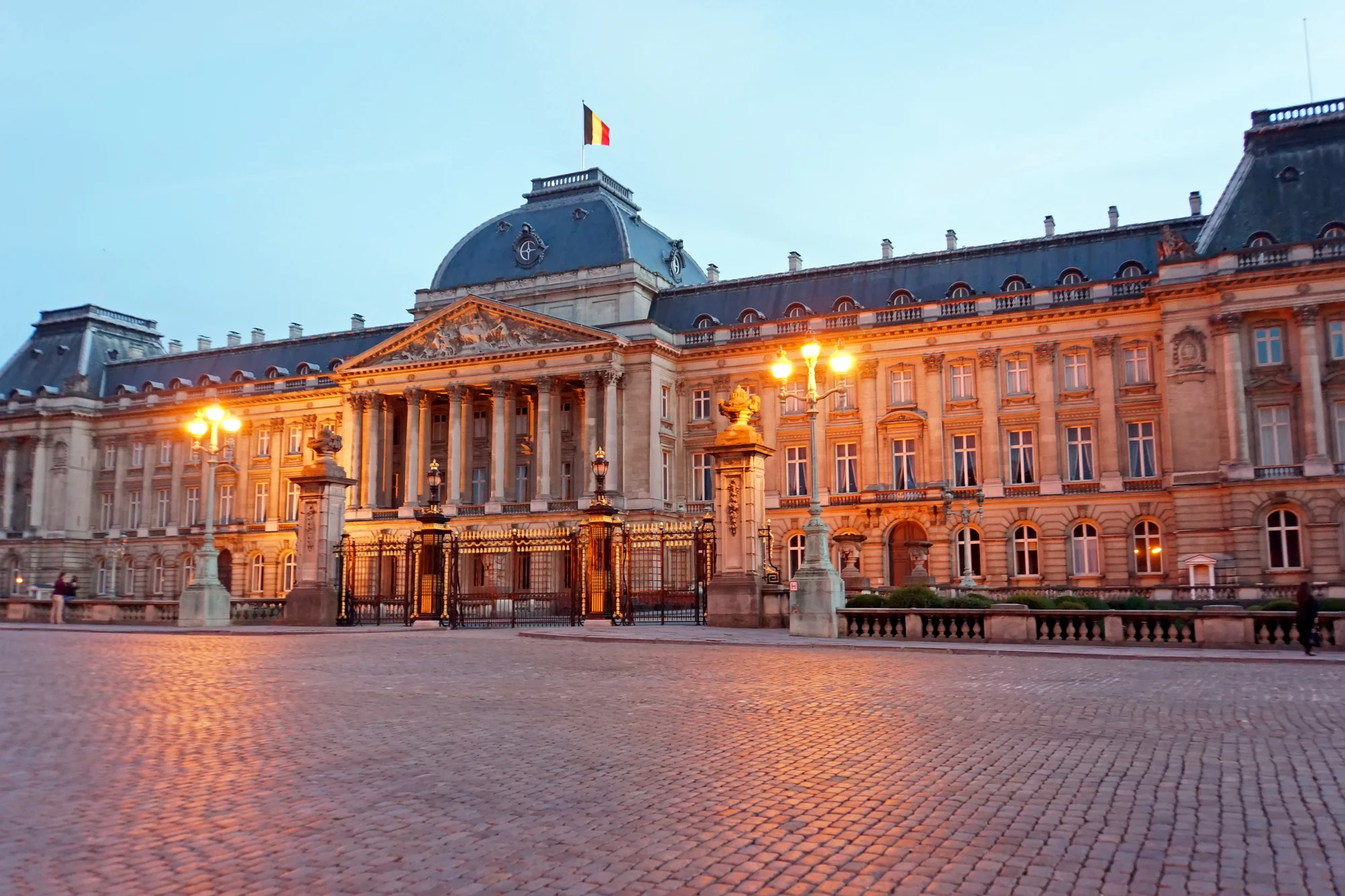 The Royal Palace of Brussels illuminated in the evening, featuring architectural details and the Belgian flag.