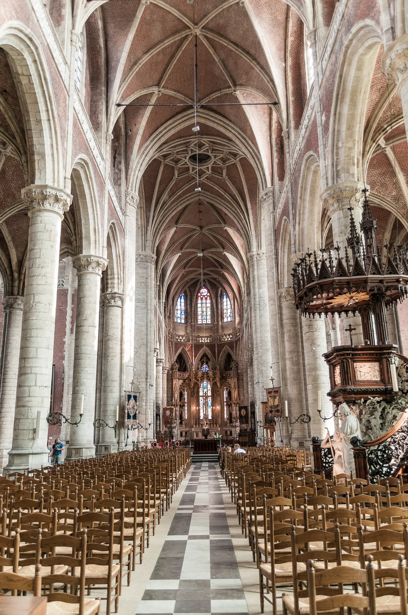 Interior of St Bavo's Cathedral in Ghent featuring towering columns and colorful stained glass windows.