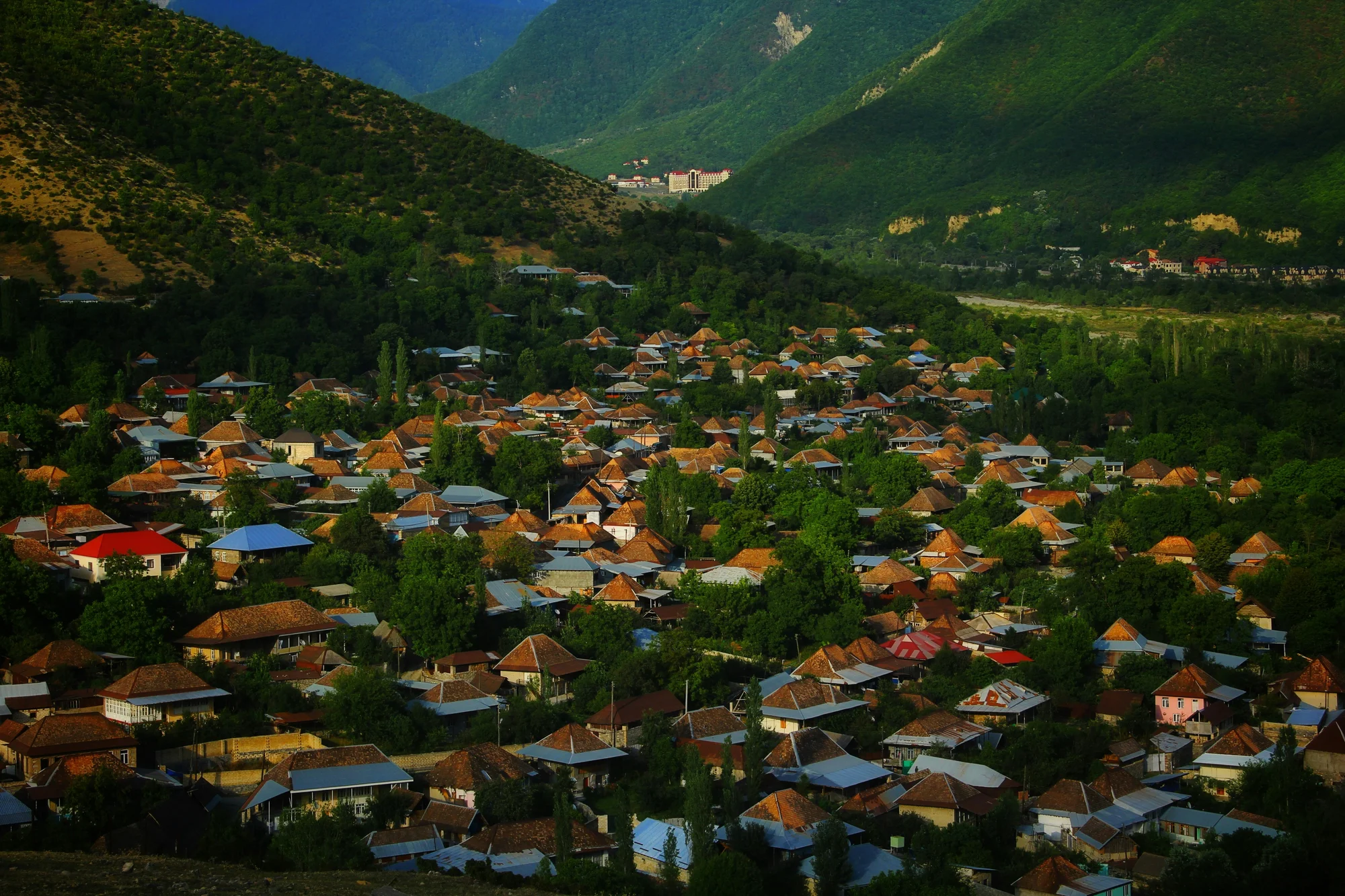 Panoramic view of Sheki city in Azerbaijan with traditional rooftops and forested hills in the background.