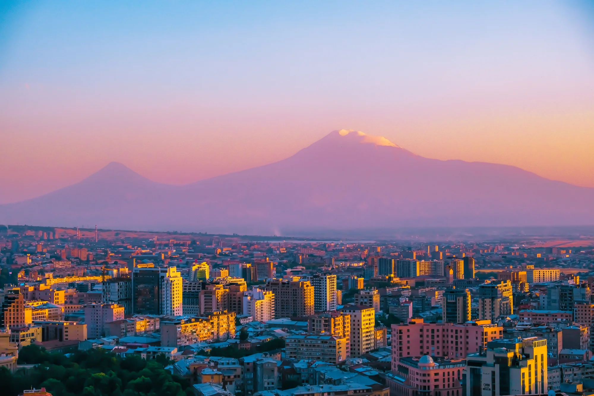 Yerevan city at sunset with Mount Ararat in the background in shades of pink and blue.