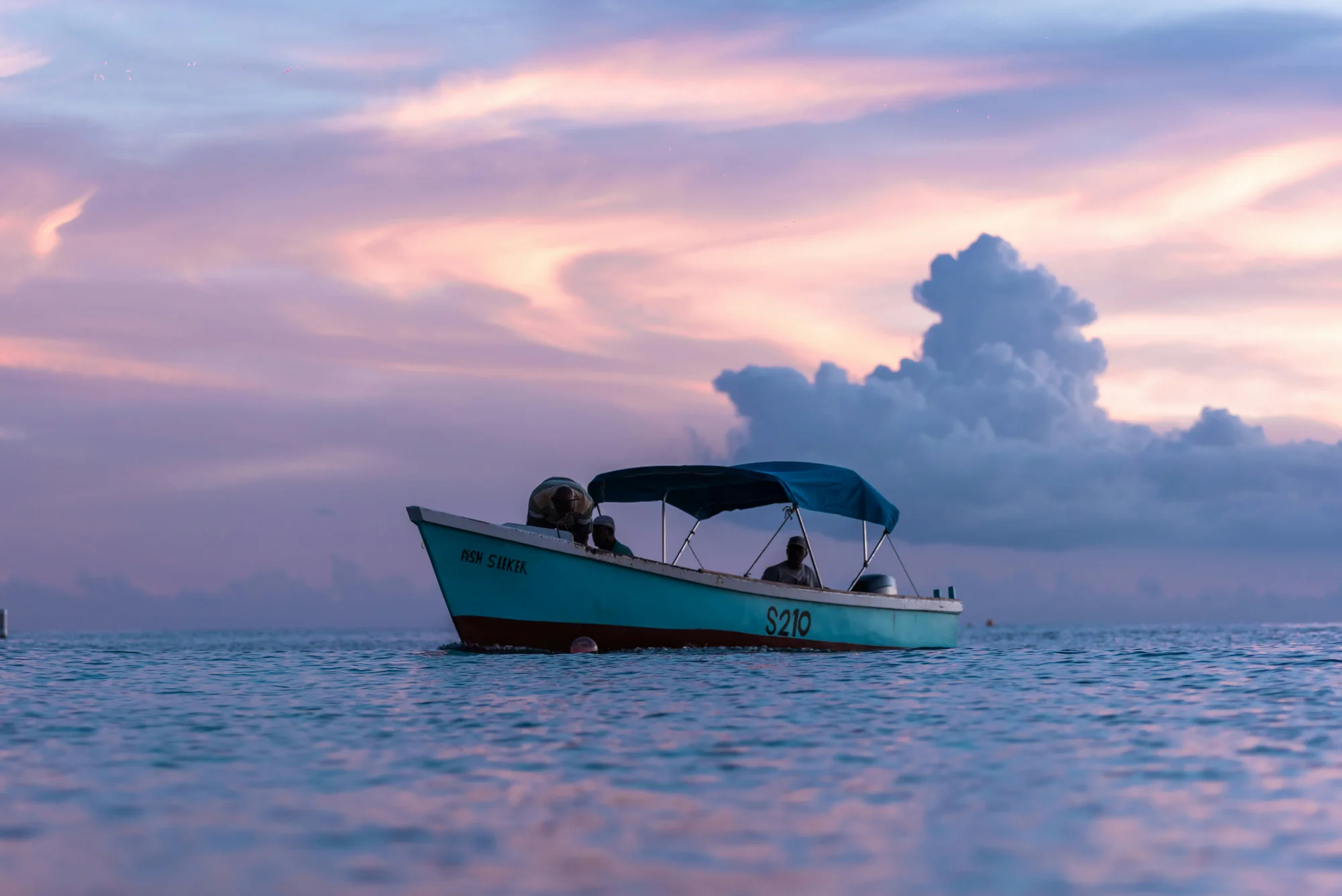 Blue boat floating on calm waters under a colorful sunset in Holetown, Barbados.