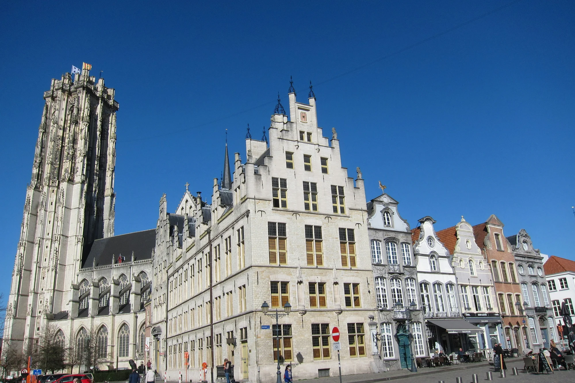 Mechelen central square with historic buildings and St. Rumbold’s Cathedral Tower under a clear blue sky.