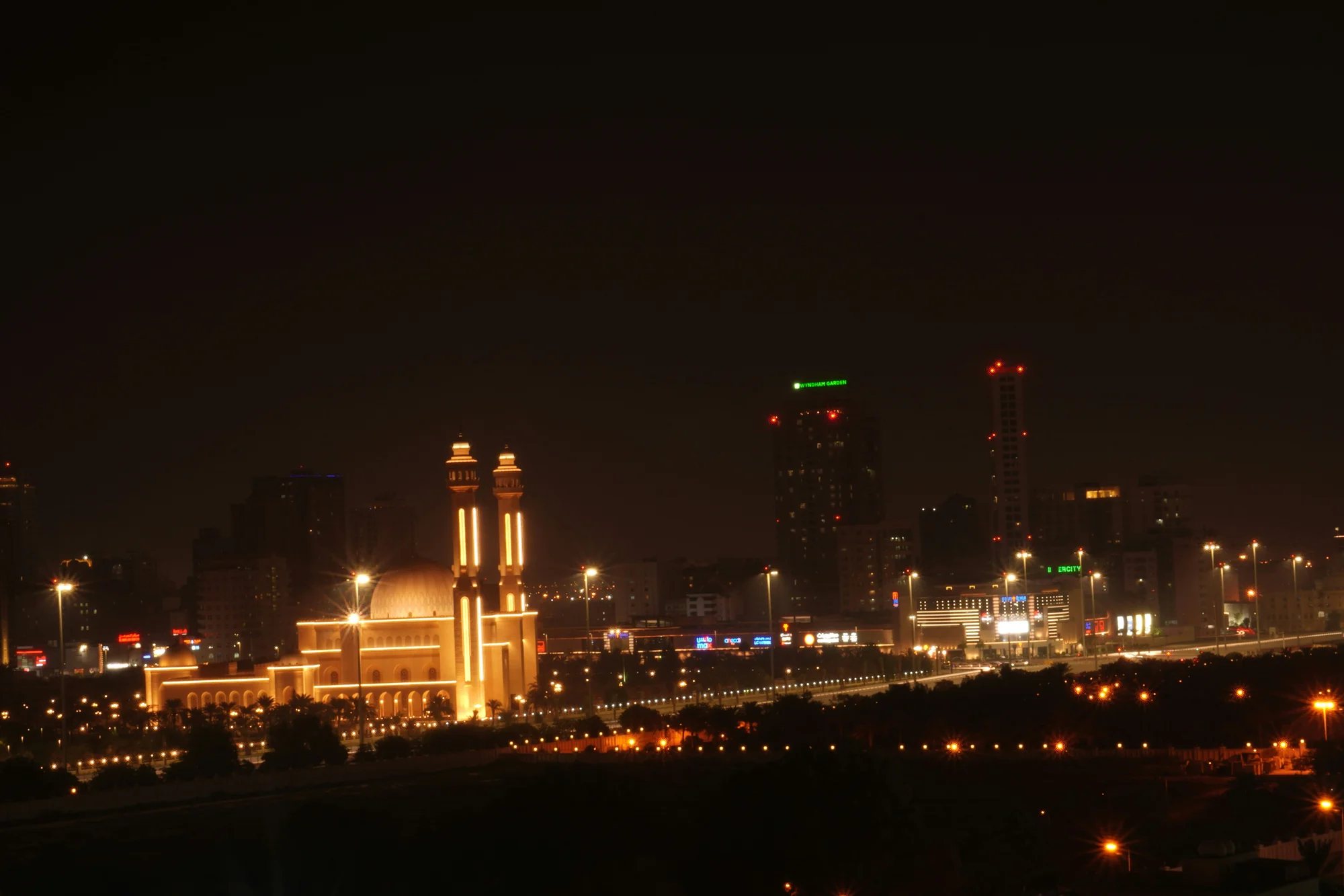 Night view of Riffa city with a lit mosque and skyscrapers in the background.