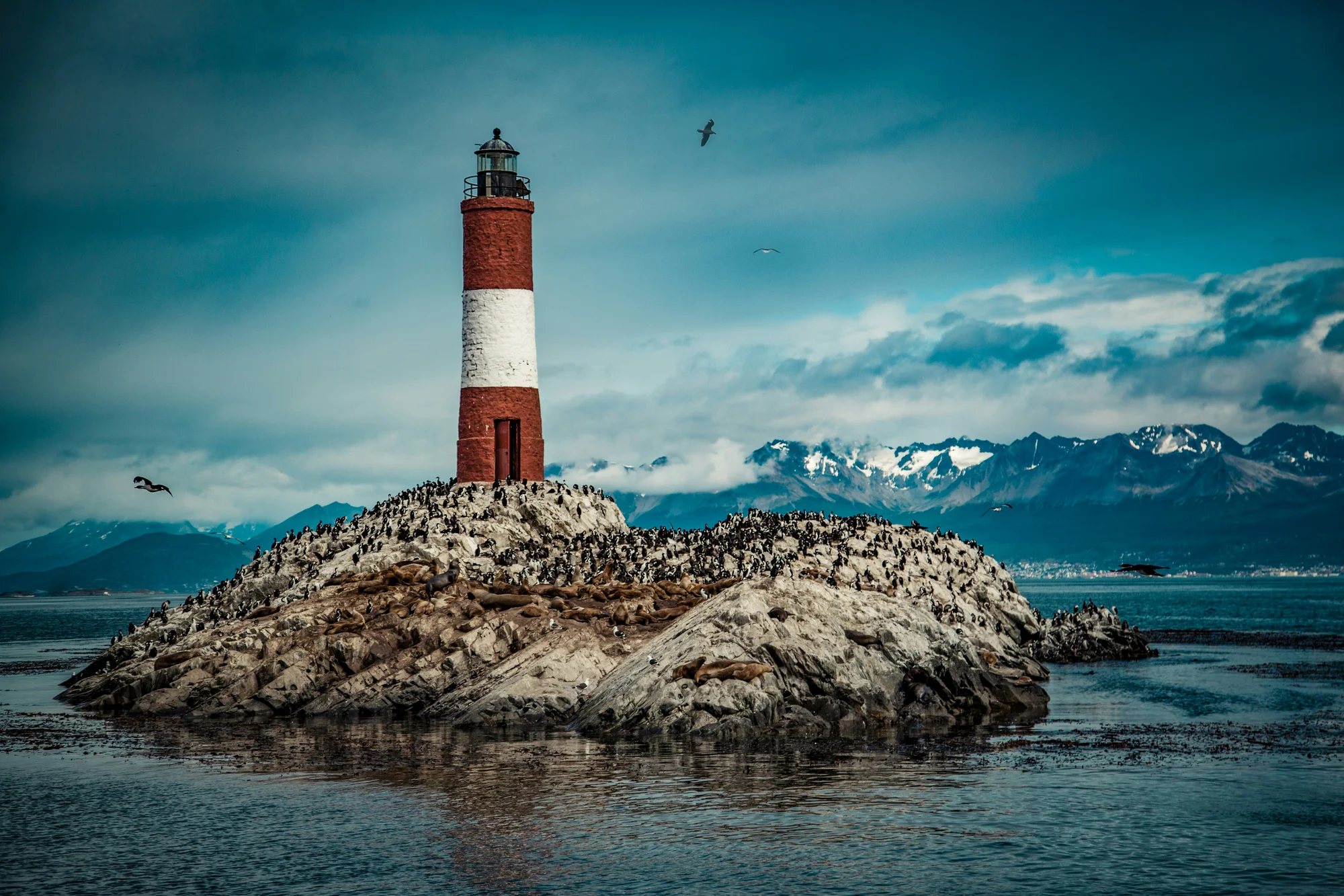 Image of the Les Eclaireurs Lighthouse in Ushuaia, perched on a rocky island with mountains in the background.