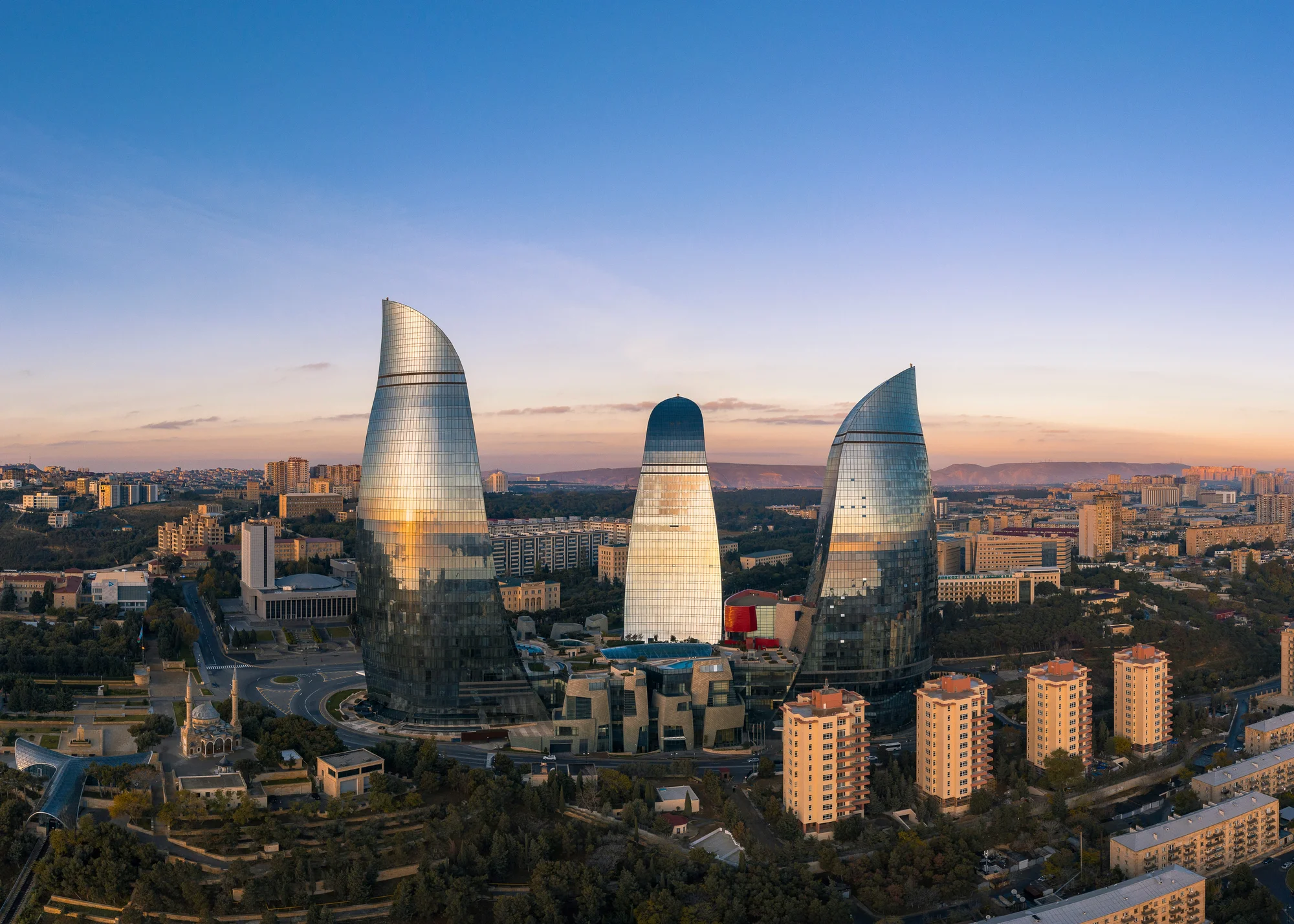 The Flame Towers in Baku captured at sunset, surrounded by modern buildings and urban scenery.