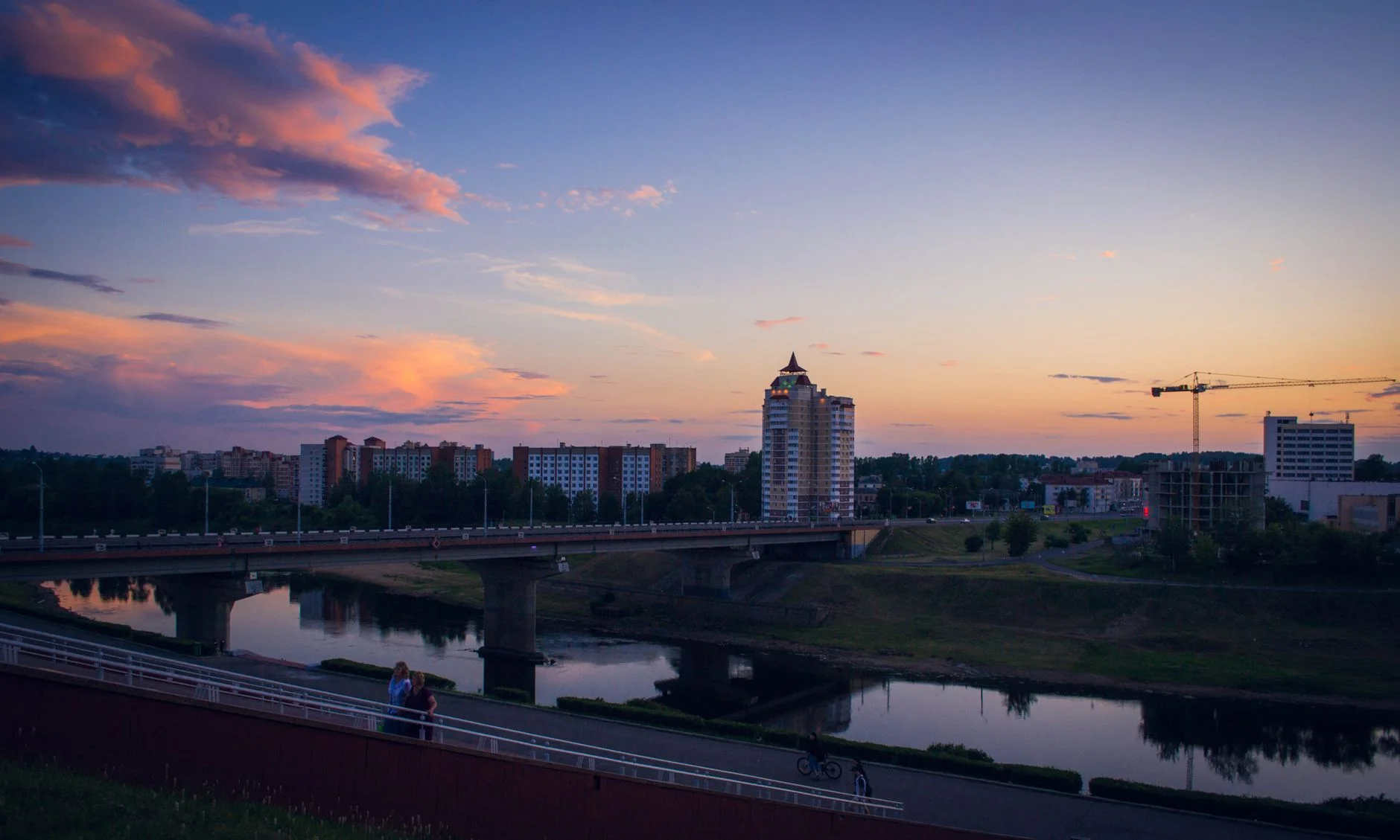 Sunset over Vitebsk, Belarus, with a bridge and modern buildings.