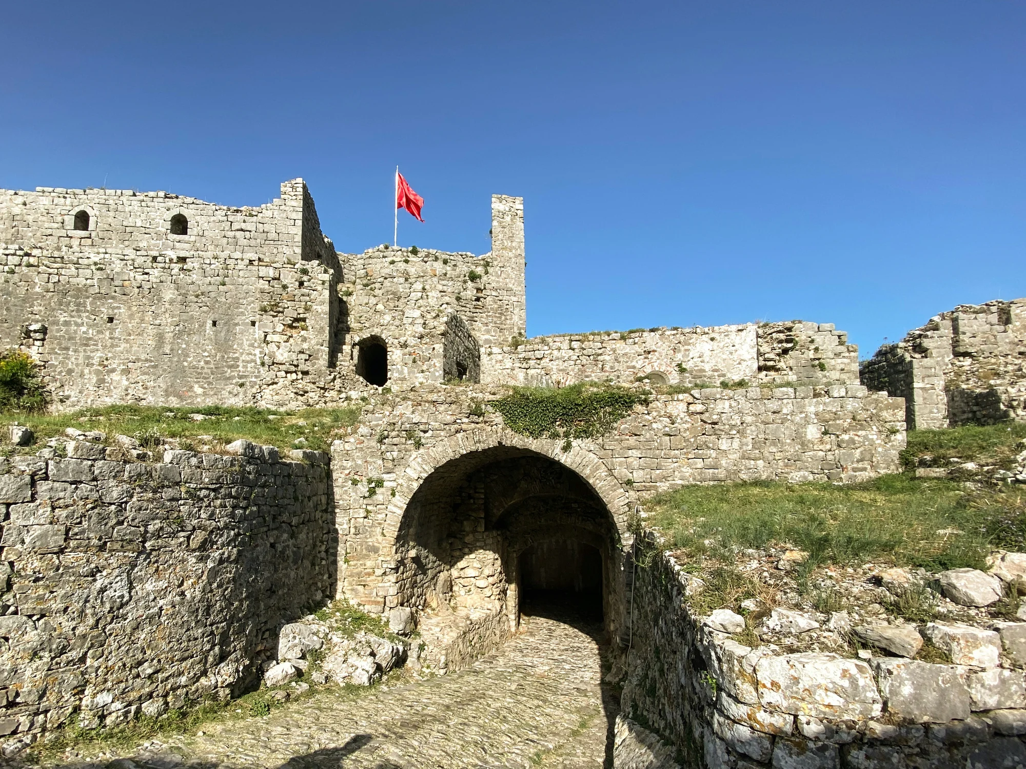 Rozafa Castle in Shkoder with the Albanian flag against a clear blue sky.