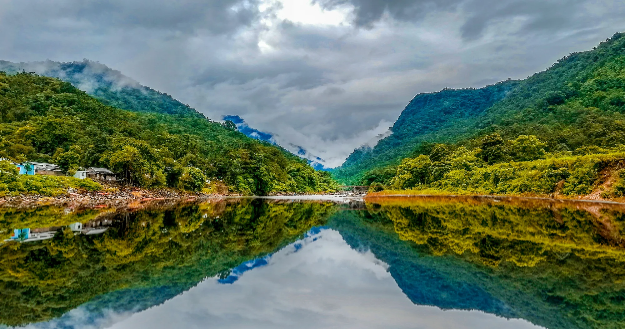 Green hills covered in lush vegetation reflected in a river in Sylhet, Bangladesh.