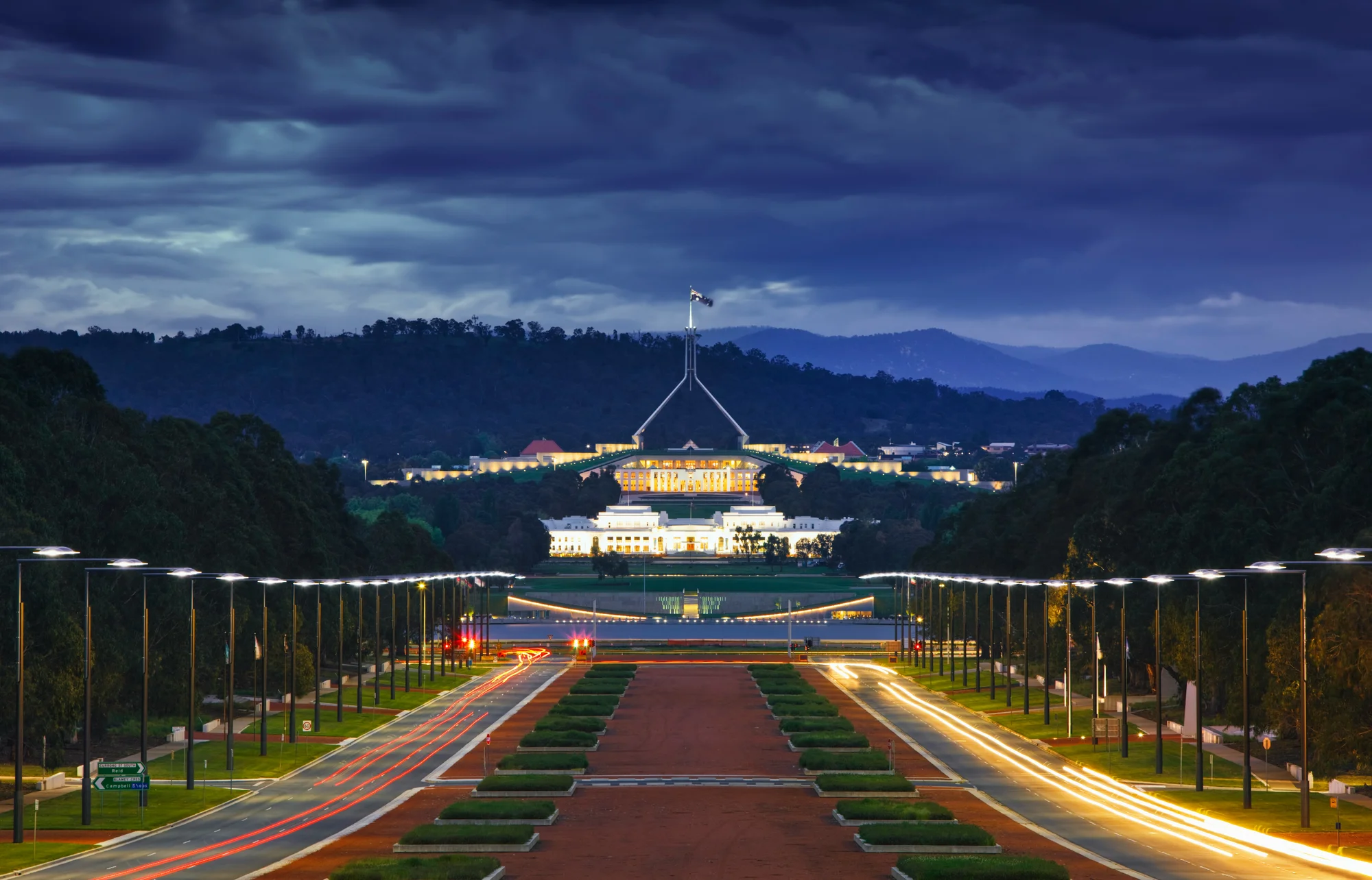 Australian Parliament at night, brightly lit with a scenic mountain backdrop in Canberra.