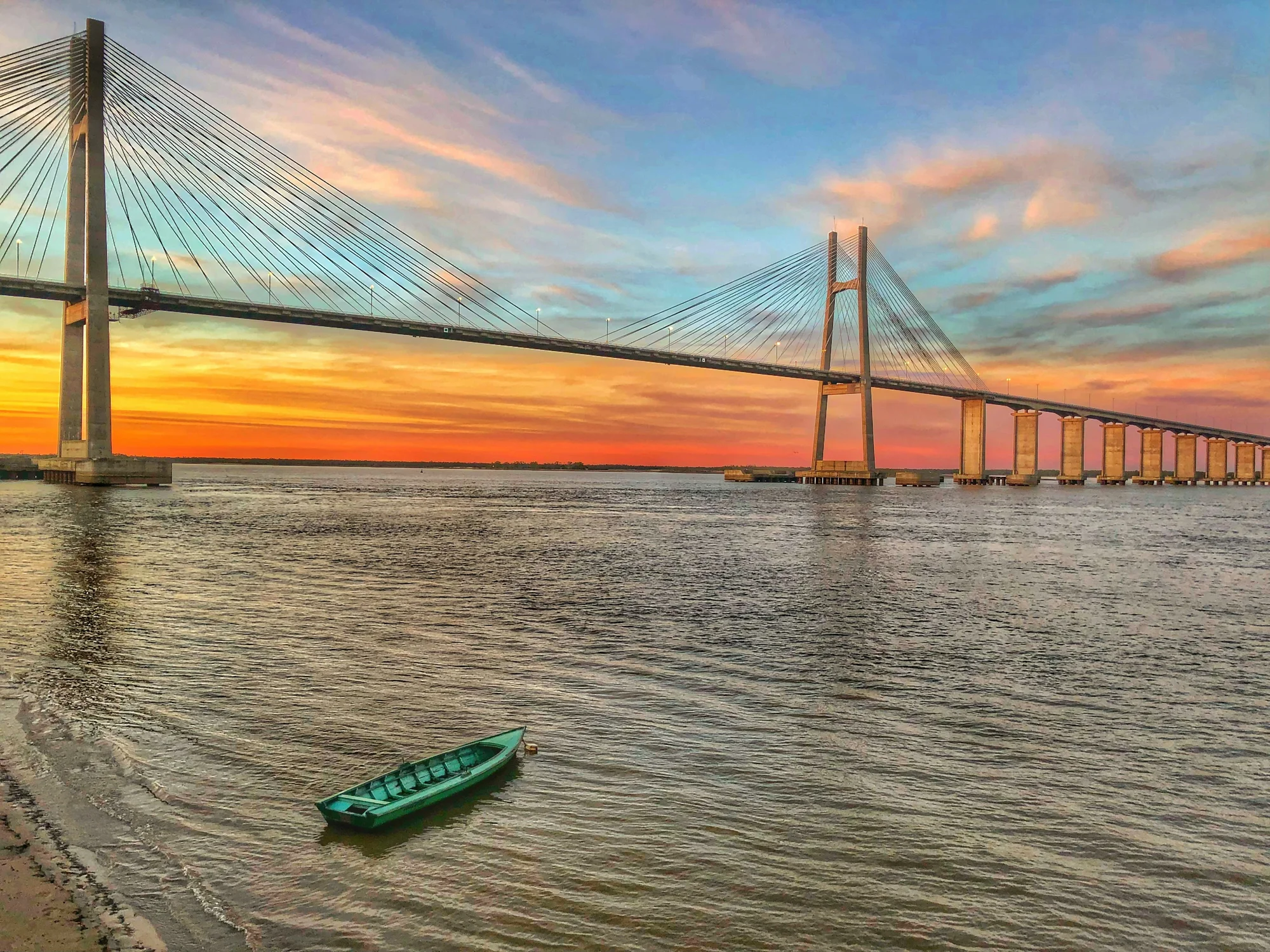 Rosario-Victoria Bridge lit by sunset with a green boat on the Paraná River.