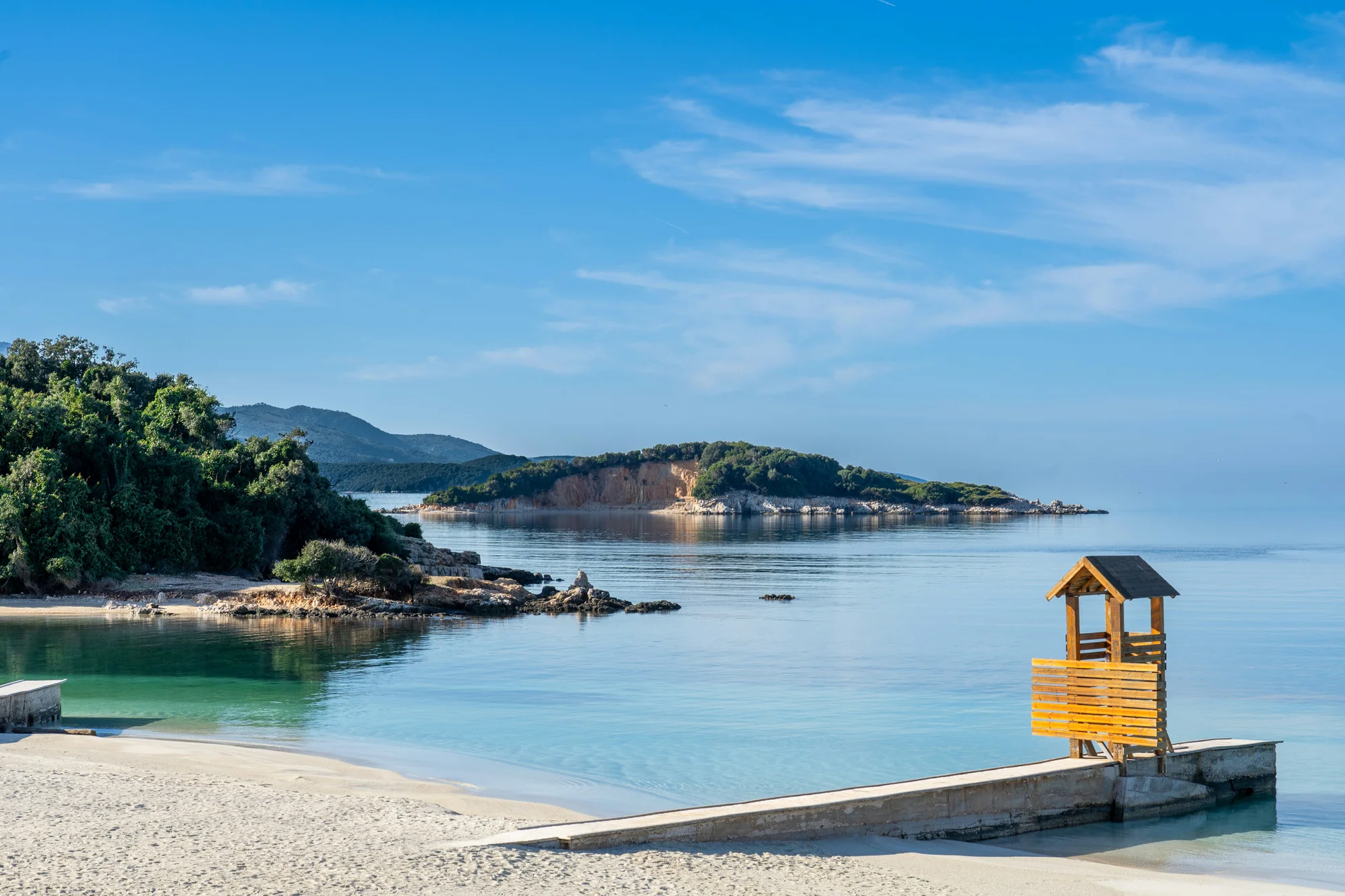 Beach in Ksamil, Albania, with crystal-clear waters, white sand, and a wooden lookout.