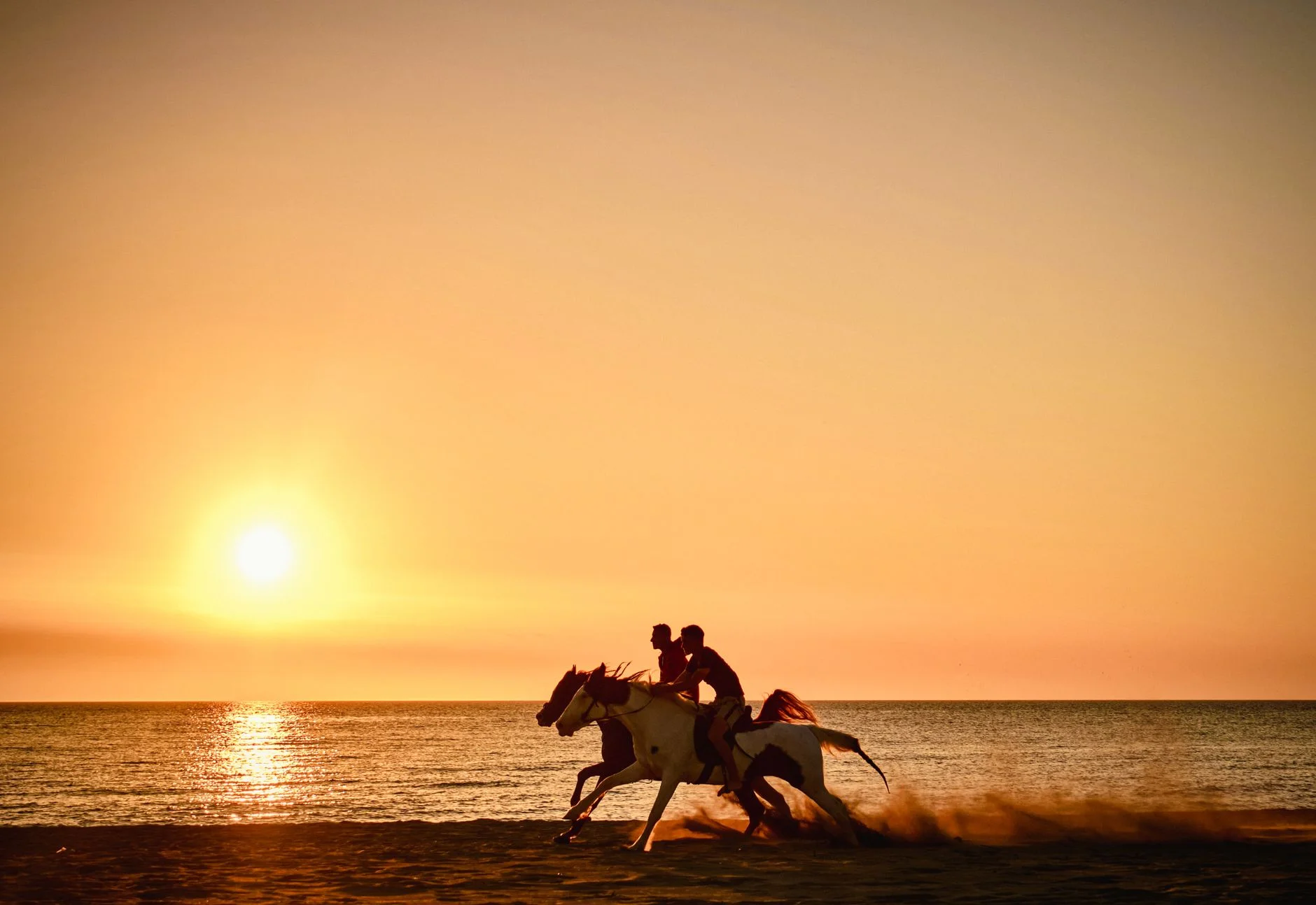 Sunset on the beach in Durres, Albania, featuring two horseback riders galloping at the shoreline.
