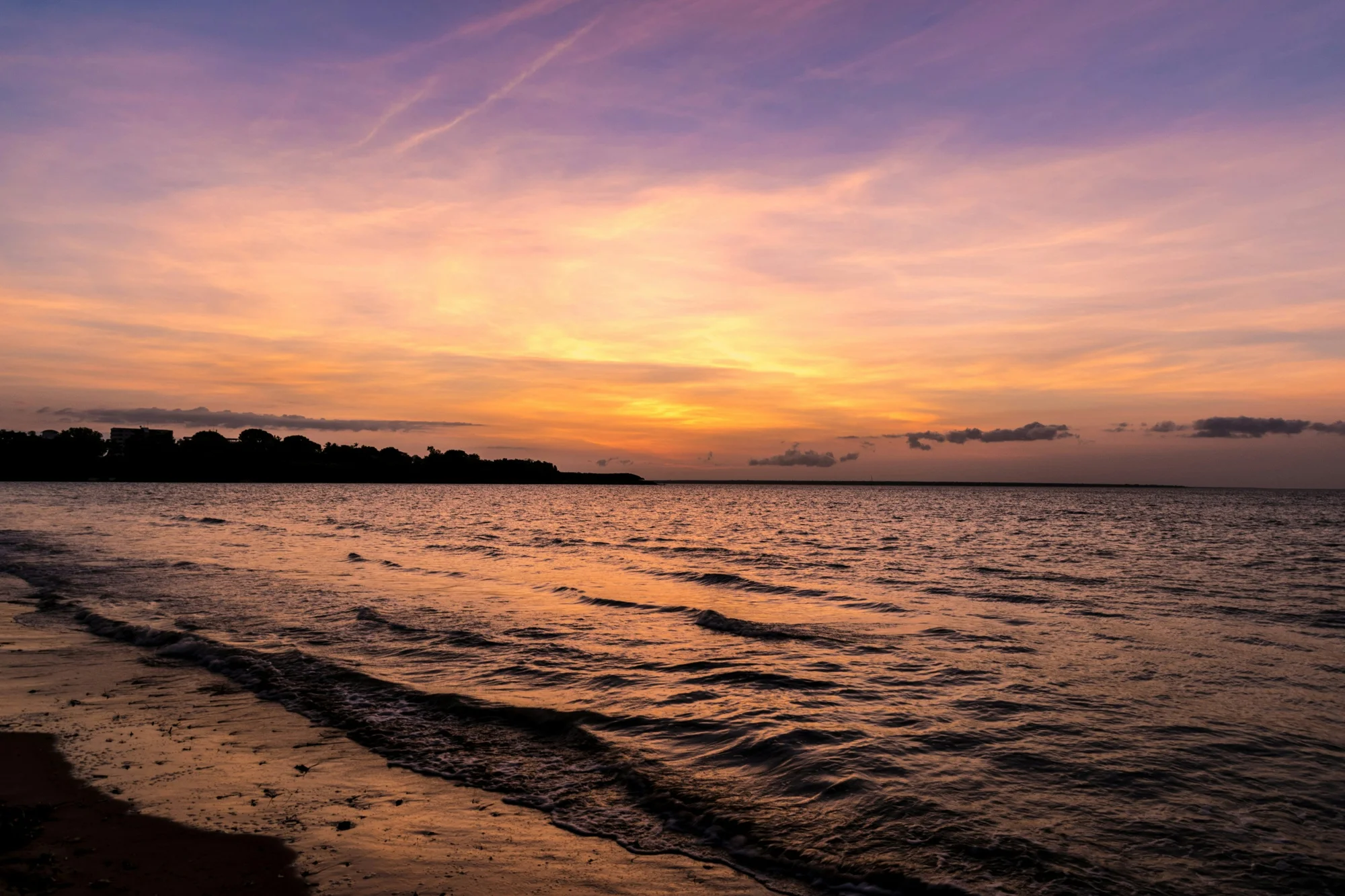 Sunset at the beach in Darwin, Australia, with colorful skies and gentle waves.