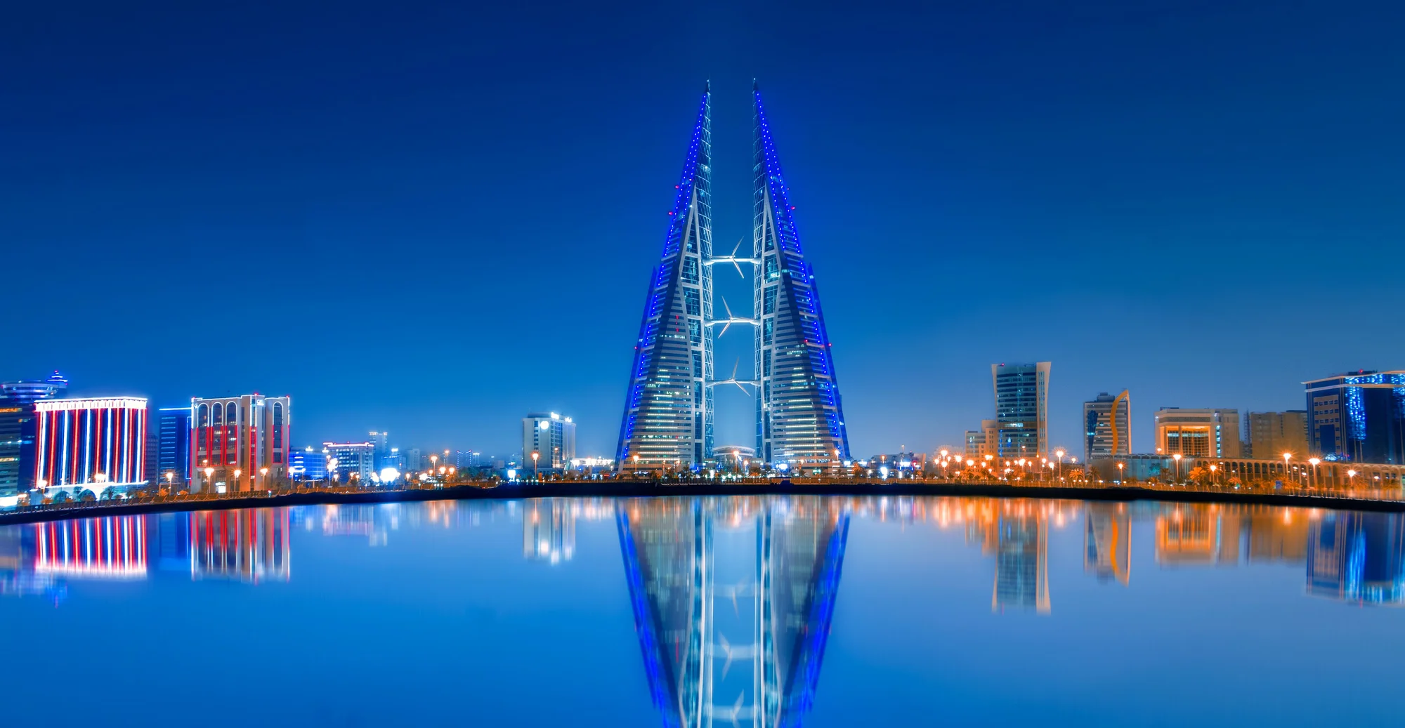 Bahrain World Trade Center Towers illuminated at night in Manama, Bahrain, reflected in the water.